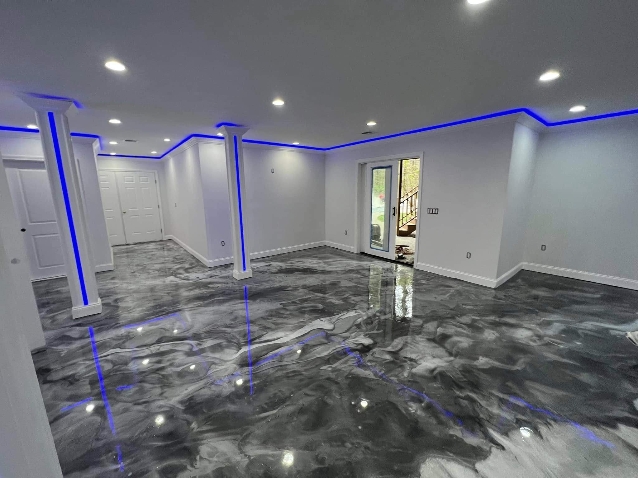 Open residential basement with a grey metallic epoxy floor under blue cove lighting