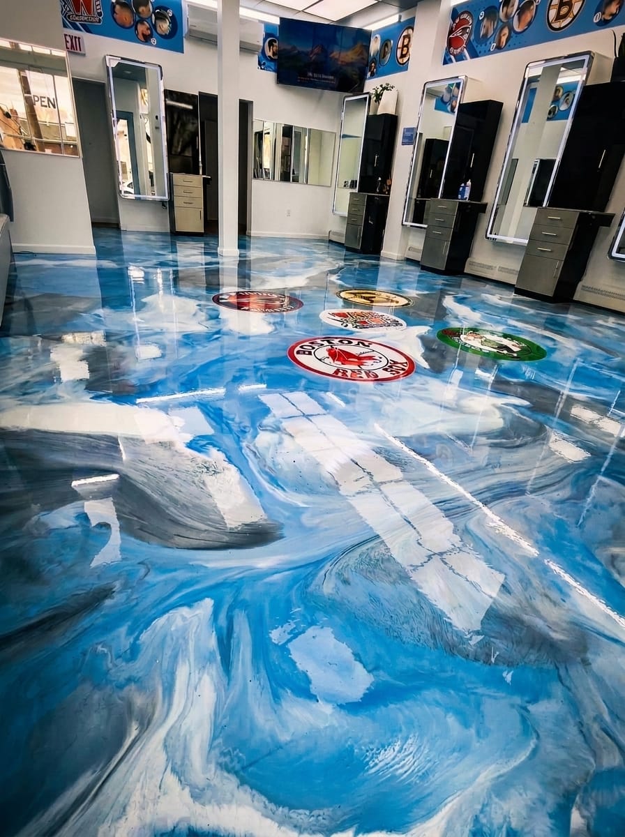 The same barbershop after: a glossy blue and white metallic epoxy floor with inlaid team logos
